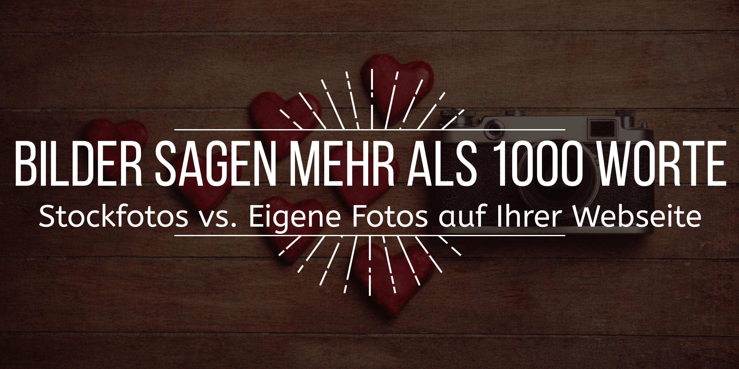 Bild mit dem vorgelagerten Text "Bilder sagen mehr als 1000 Worte Stockfotos vs Eigene Fotos auf Ihrer Webseite" - im Hintergrund ein Fotoapparat neben mehreren roten gezeichneten Herzen auf einem schönen alt wirkenden Holzboden